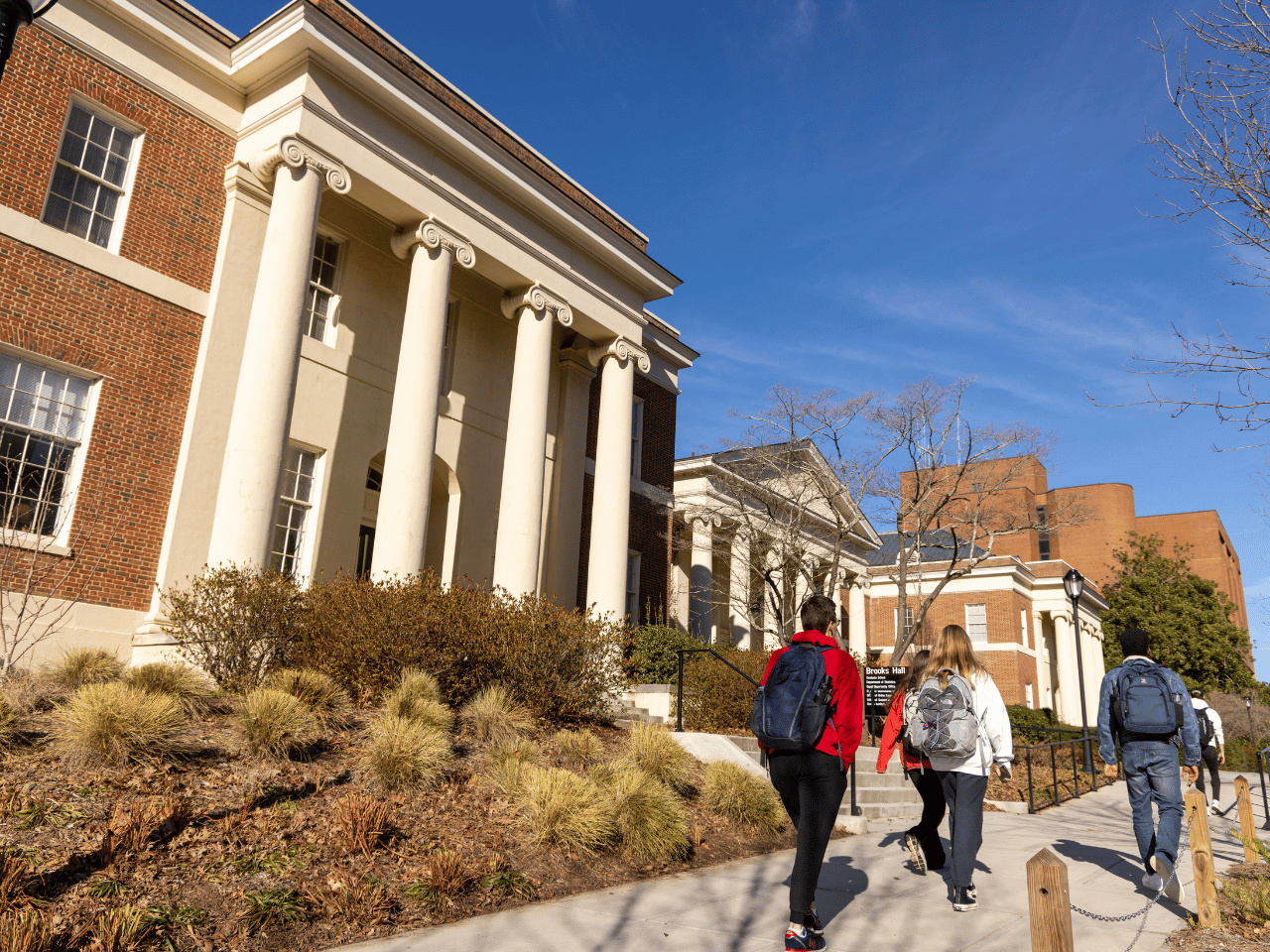 View of students walking on the sidewalk in front of the Brooks Hall south entrance on a sunny winter day.